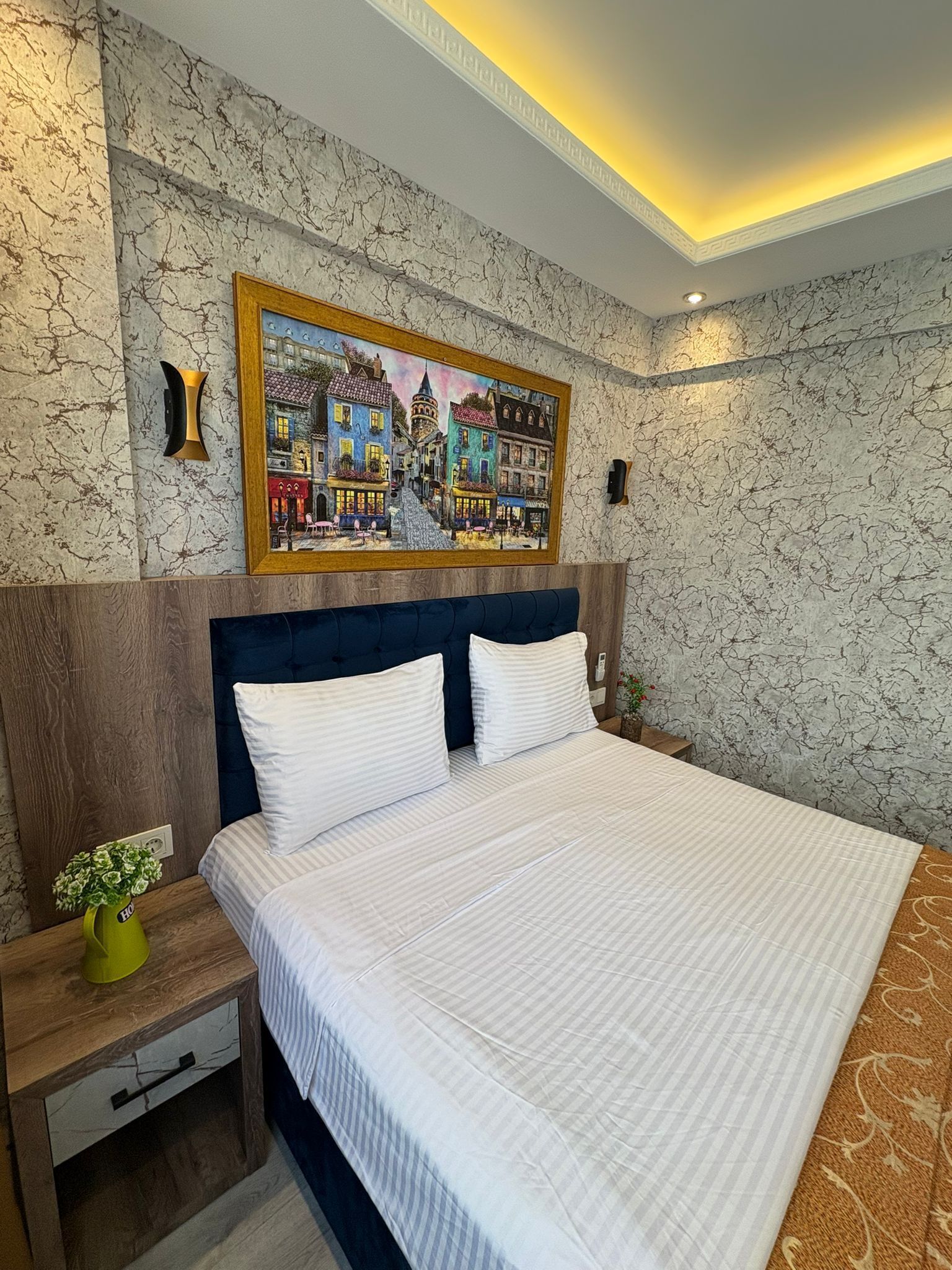 A neatly made bed with white linens, a wooden headboard, and a nightstand with a green vase.