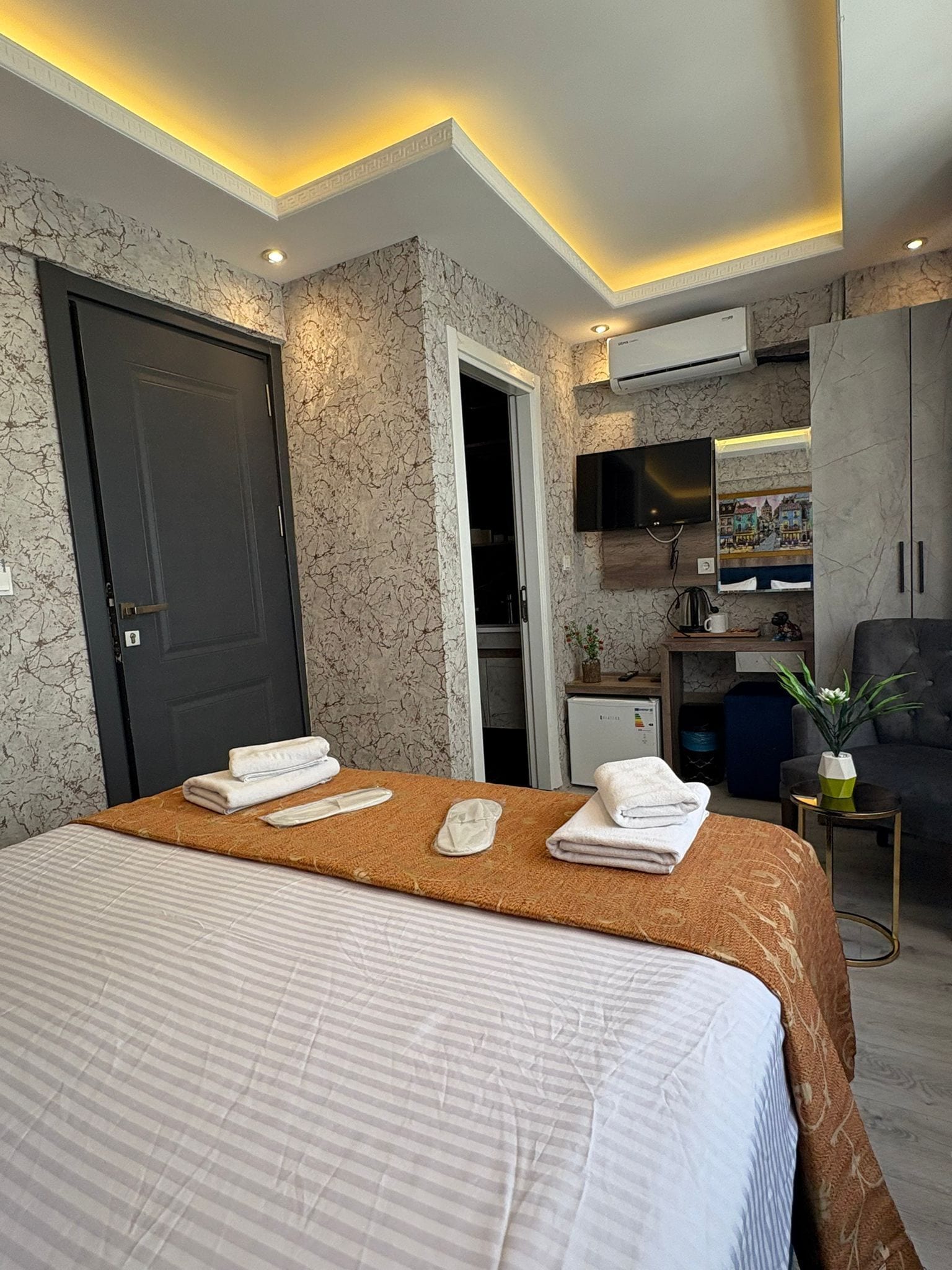 Ein Hotelzimmer mit Bett, Handtüchern, Fernseher, Schreibtisch mit Pflanze und Kleiderschrank.