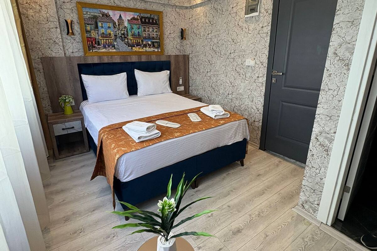 Una habitación de hotel moderna con una cama grande, una mesita con una planta y una puerta.
