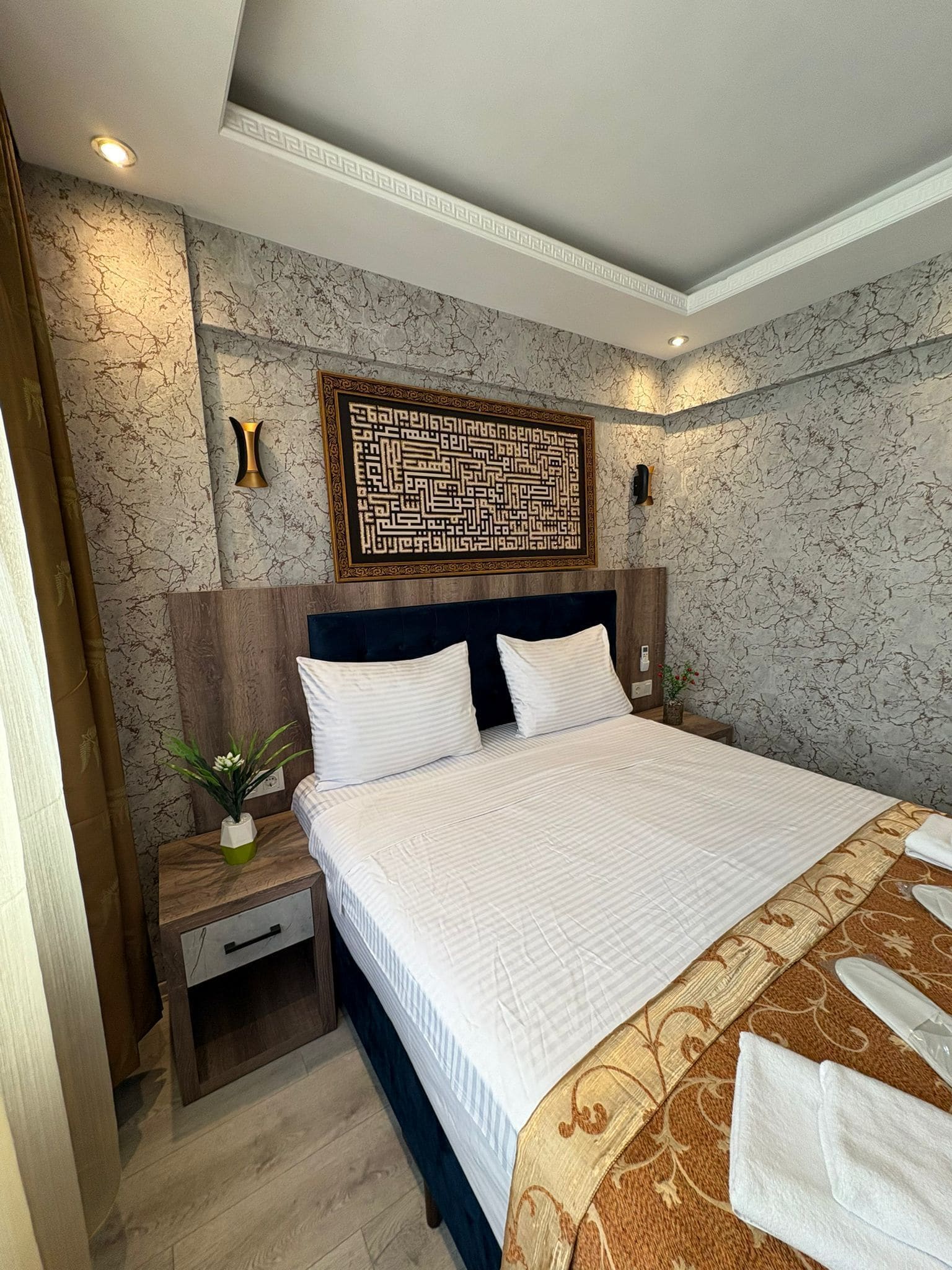 Una cama bien hecha con sábanas blancas, cabecera oscura y un adorno decorativo encima.