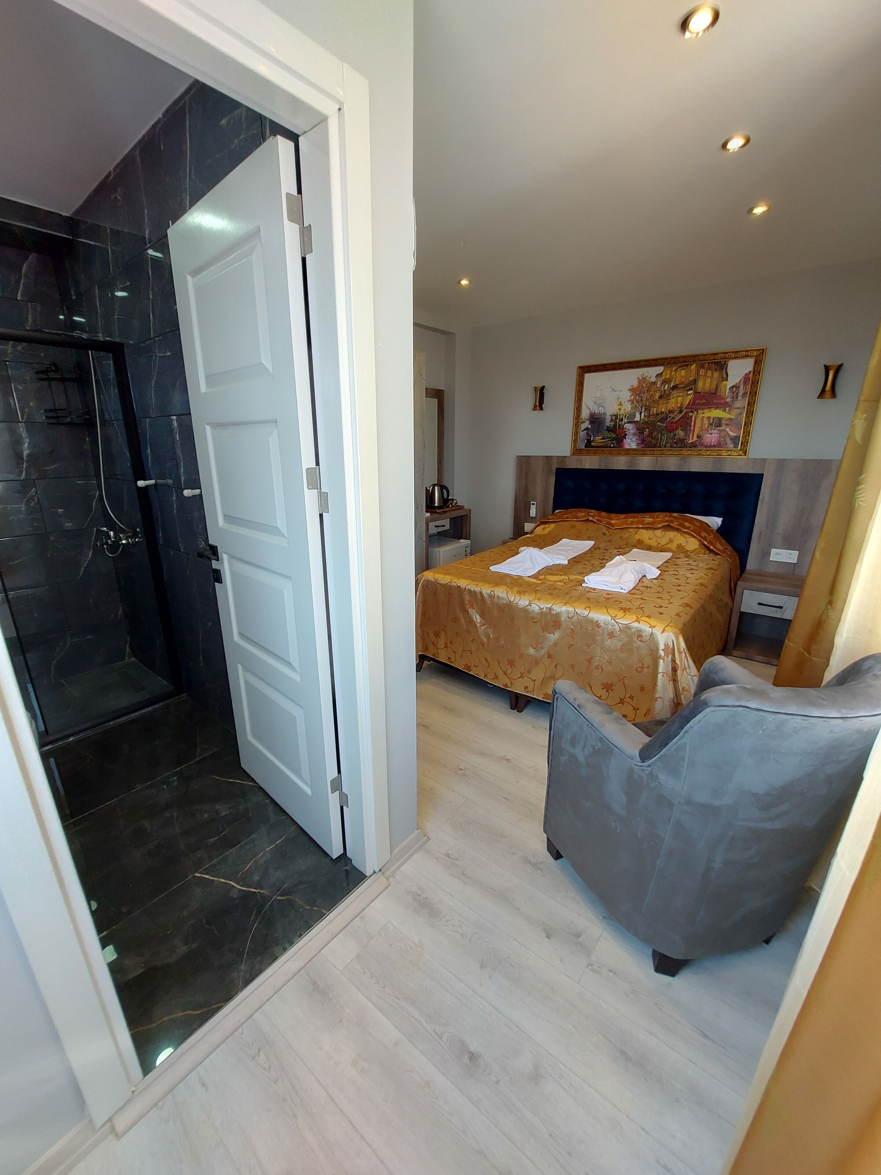 A hotel room with a bed, a shower area, a desk, and a painting on the wall.