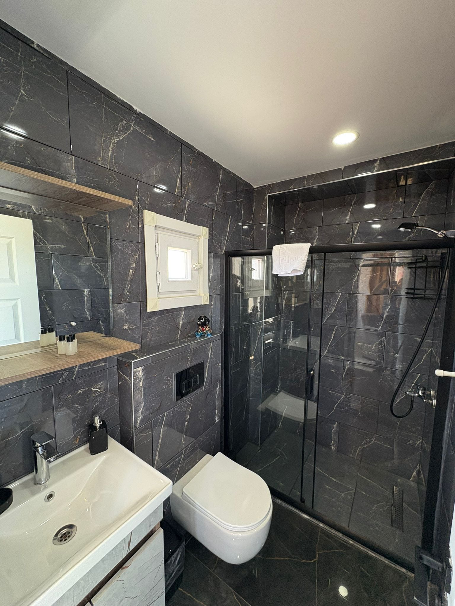 A modern bathroom with a marble backsplash, a white sink, a toilet, and a glass-enclosed shower.