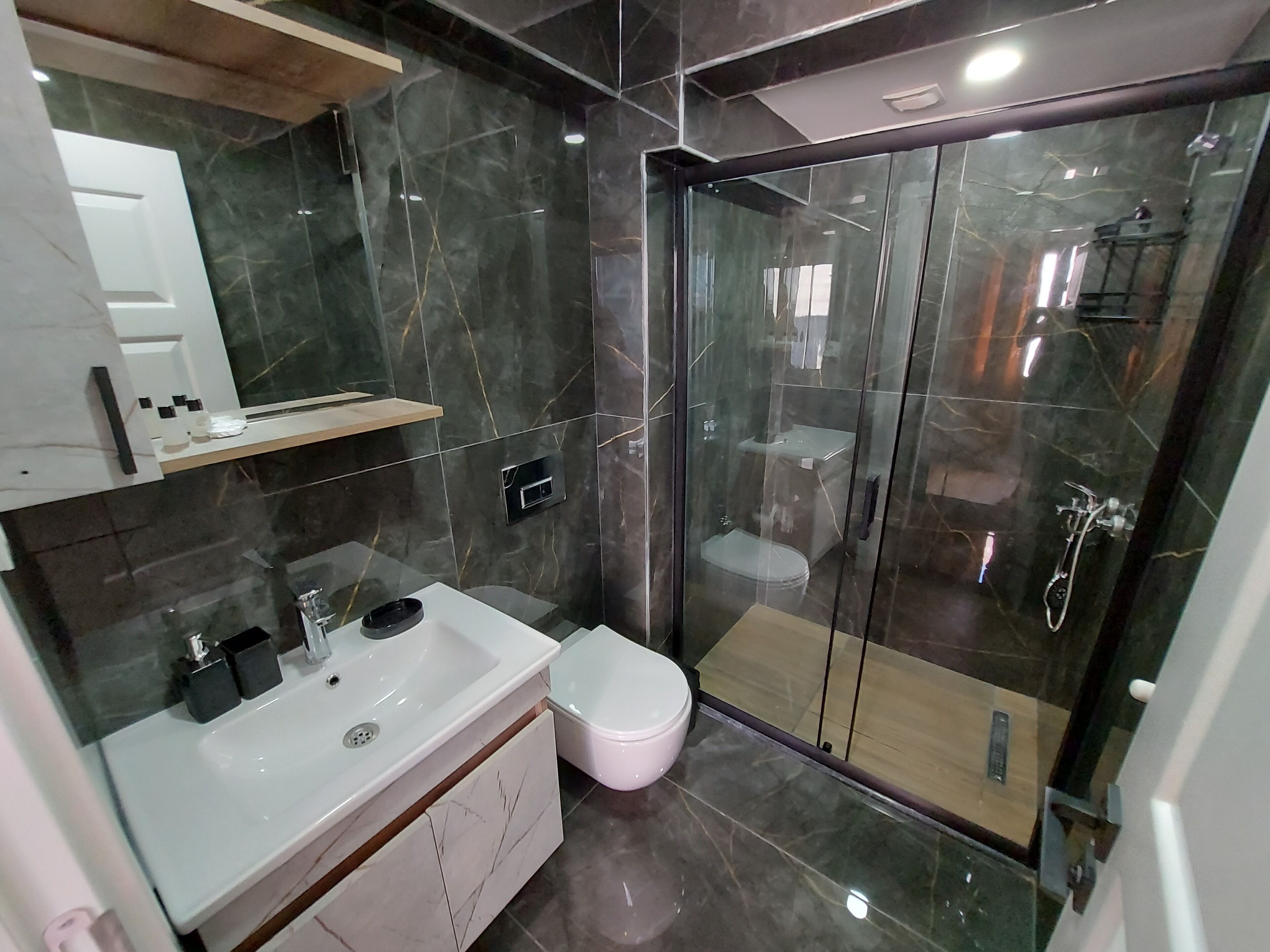 A modern bathroom with a glass-enclosed shower, a white sink, and a toilet.
