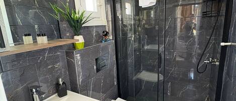 A modern bathroom with a marble floor, a white sink, a toilet, and a glass-enclosed shower area.