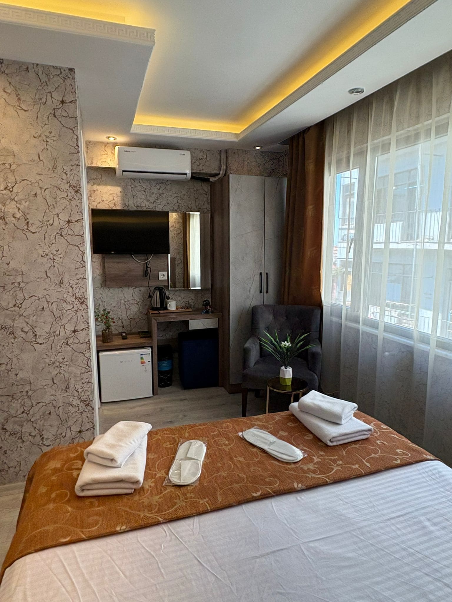 Une chambre d’hôtel avec un lit, un bureau, une chaise, une télévision et une fenêtre avec des rideaux.