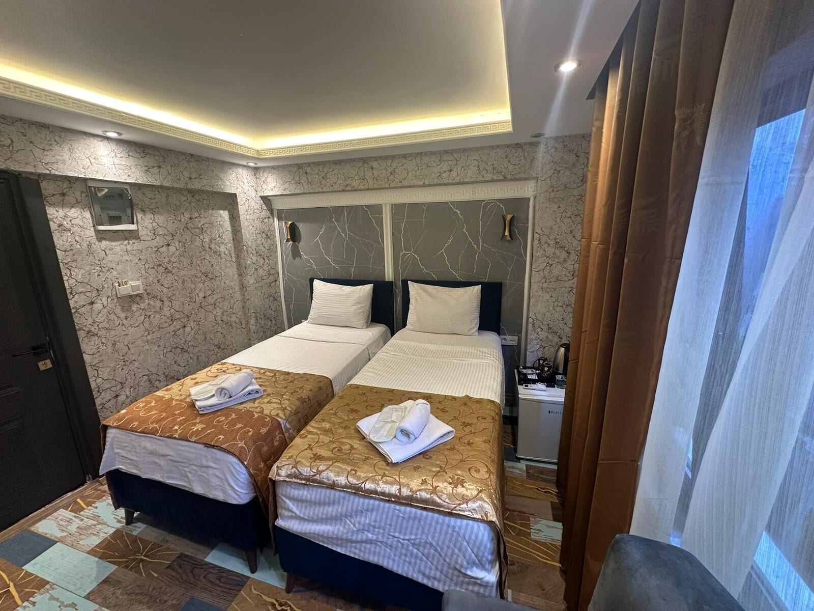 A hotel room with two beds, marble walls, and a modern ceiling design.