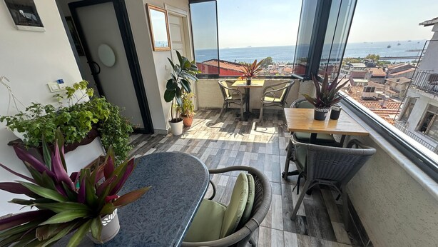 Ein Balkon mit Tisch, Stühlen, Topfpflanzen und Blick auf das Meer und Gebäude.