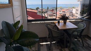Ein Balkon mit Blick auf das Meer und Gebäude. Ein Tisch mit Stühlen und einer Topfpflanze ist vorhanden.