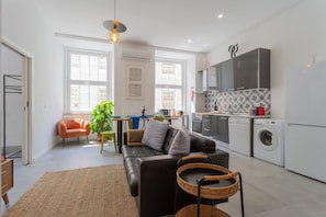 A modern kitchen with a washing machine, a dining area with a sofa, and a large window.
