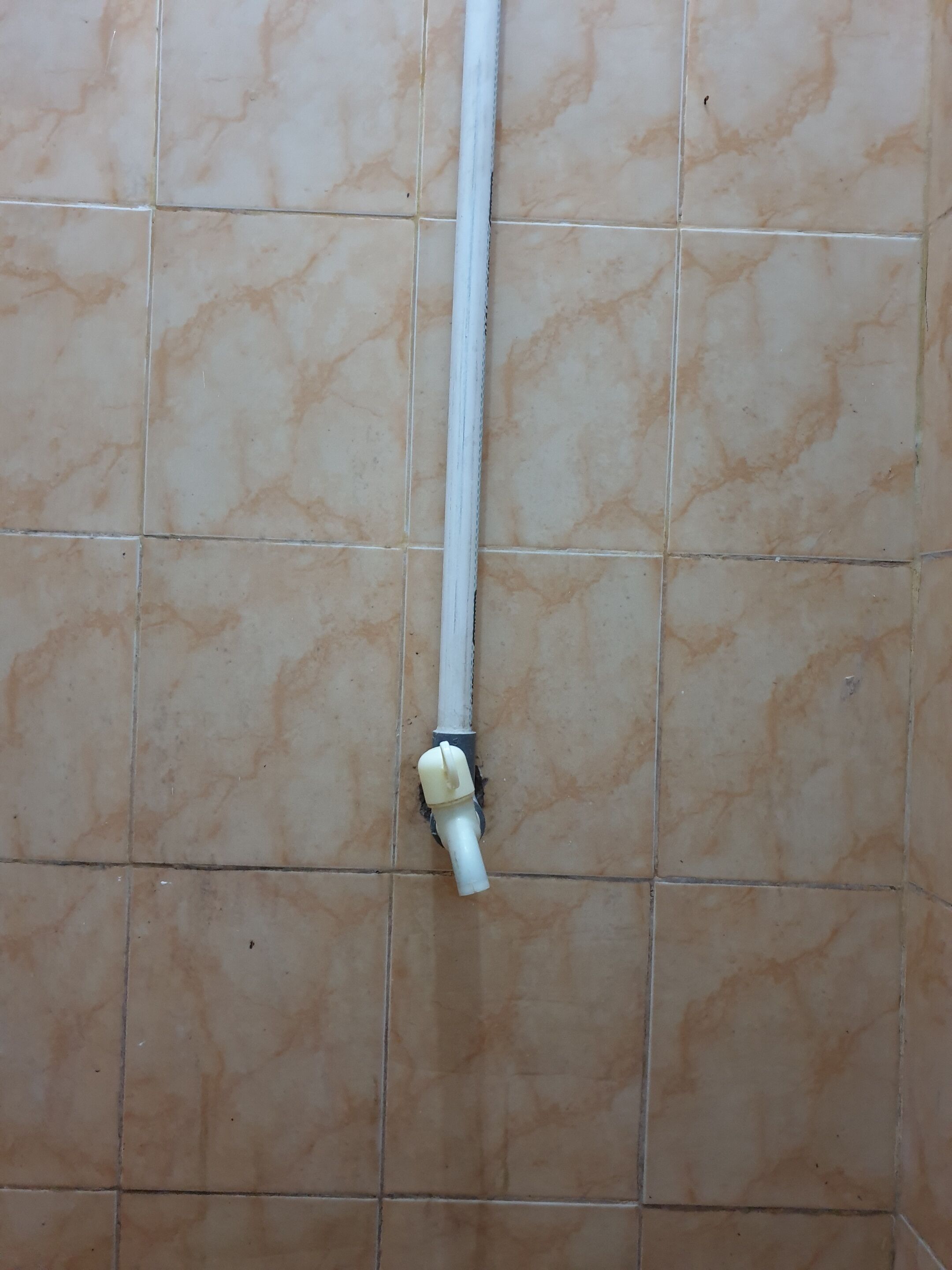A bathroom with beige tiled walls and a white pipe running vertically.