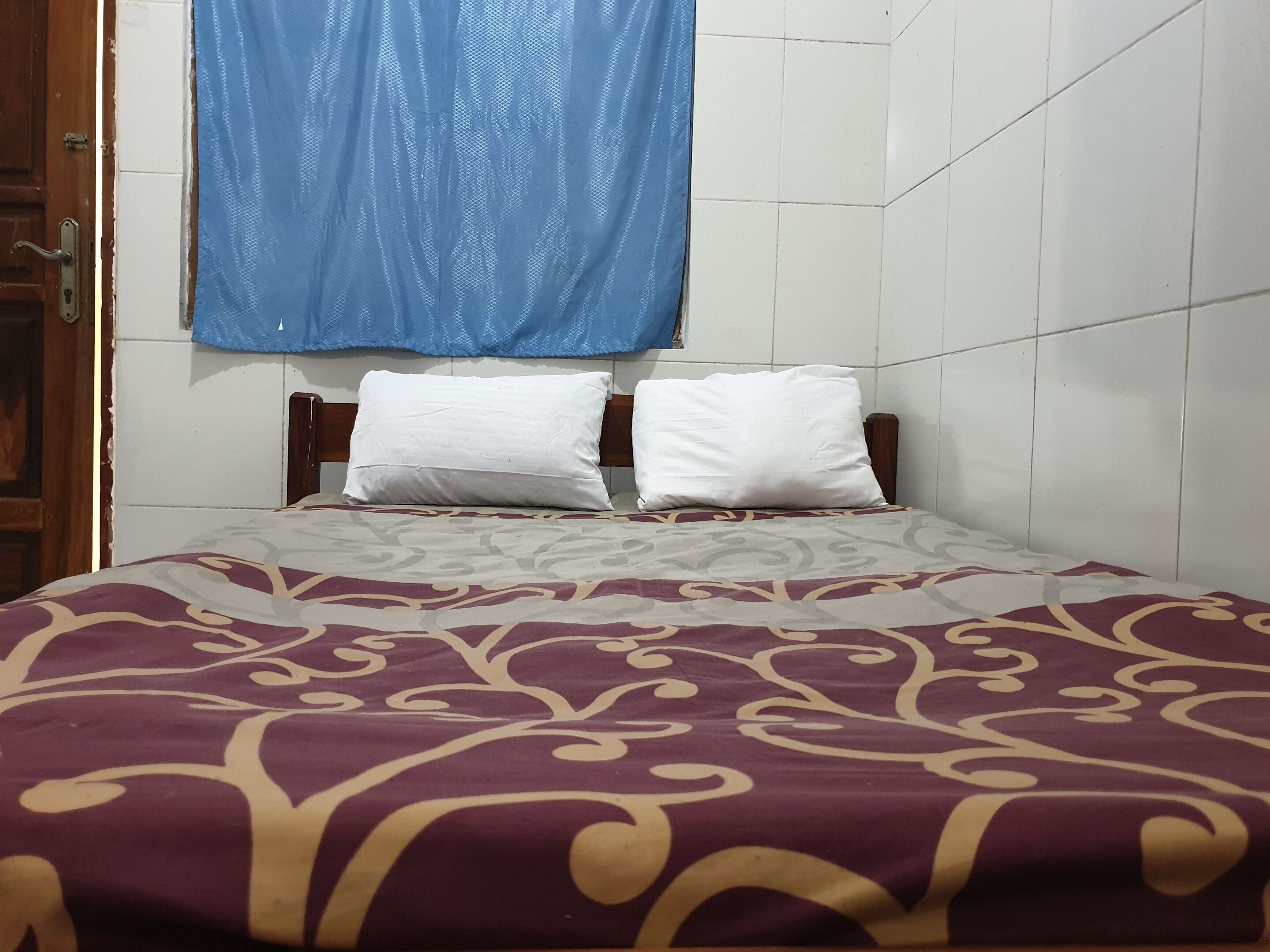 A bed with a patterned bedspread, two white pillows, and a blue curtain above.