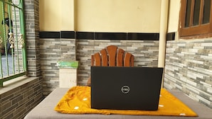 A laptop on a table with a yellow cushion, a wooden chair, and a tiled wall with a black and white border. - OYO Life  92620 Syfa Kost (Malang)