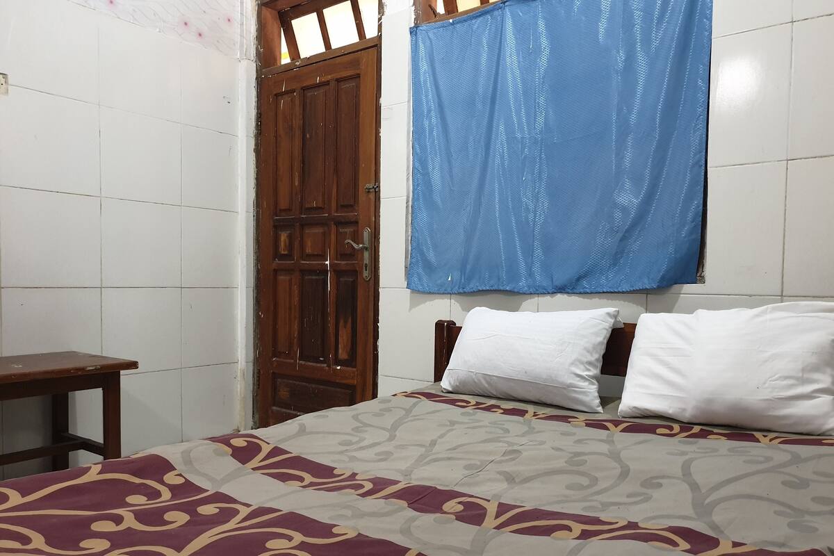 A bedroom with a bed, a wooden door, and a blue curtain.