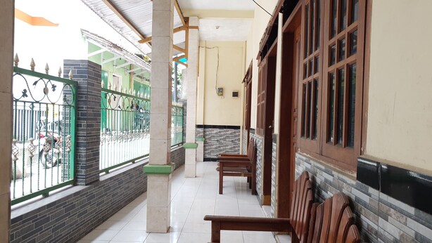 A covered corridor with tiled flooring, benches, and a green metal gate leading to a building. - OYO Life  92620 Syfa Kost (Malang)