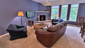 A living room with a brown leather sofa, a black armchair, a wooden coffee table, and a fireplace. - Long Lake North Periwinkle (Phillips)