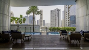 A rooftop lounge with wicker furniture, a pool, and a city view. - Elegant Apartment Amidst Vibrant Area with Balcony (Dubai)