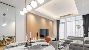 A modern living room with a dining area, a flat-screen TV mounted on the wall, and a large window with curtains. - Elegant Apartment Amidst Vibrant Area with Balcony (Dubai)