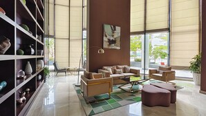 A spacious living area with a large bookshelf, comfortable seating, and large windows offering a view of the outdoors. - Elegant Apartment Amidst Vibrant Area with Balcony (Dubai)