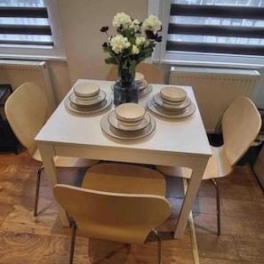 A dining table with plates and a vase of flowers, surrounded by chairs. - Central  London | Walk to Soho, Oxford St & Shops (Greater London)