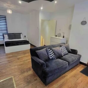 Un salon moderne avec un canapé gris, un lit blanc et un plancher en bois.