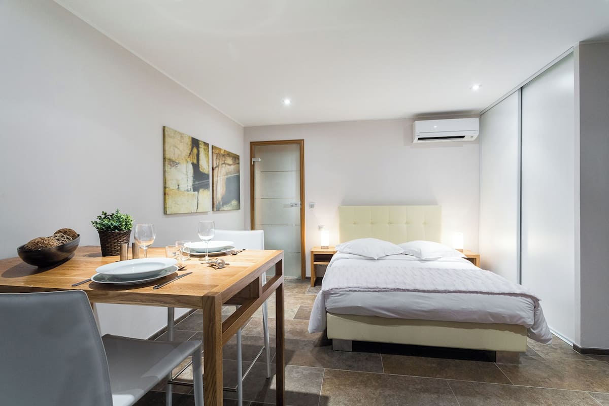 Une chambre d’hôtel moderne, équipée d’un lit, d’une table de chevet et d’un coin repas avec une table, des chaises et un saladier rempli de fruits.