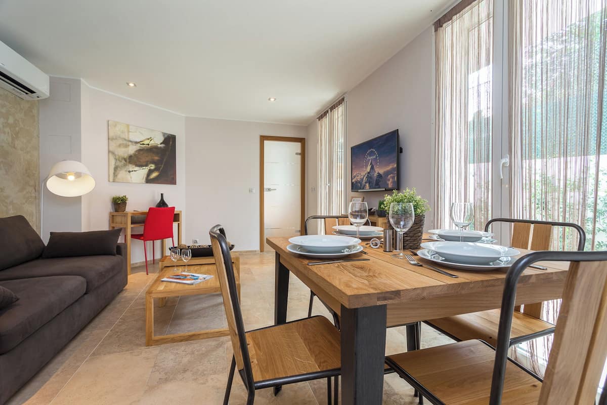 Un salon moderne avec un canapé, une table à manger dressée pour quatre personnes et un fauteuil rouge.