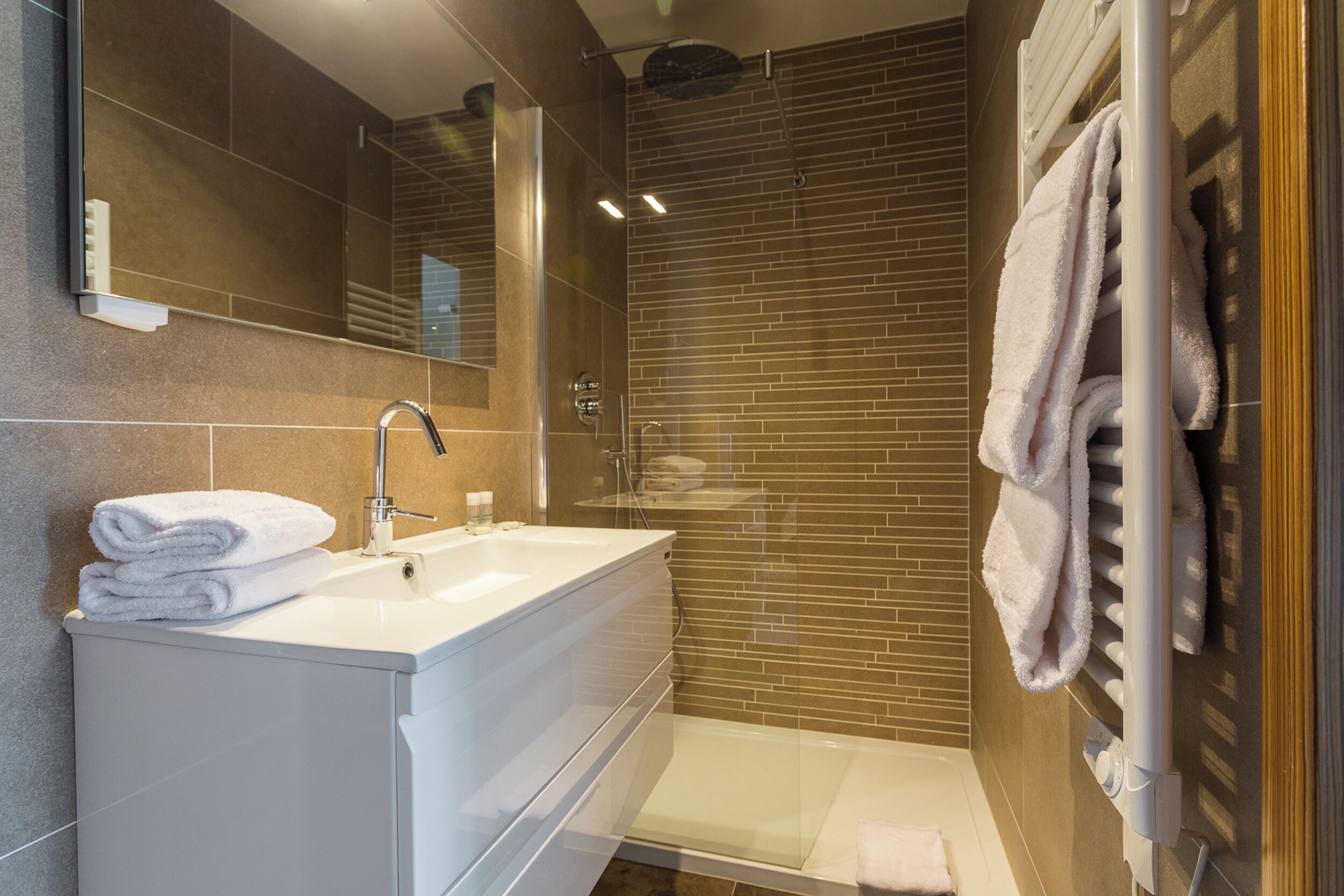 Un baño moderno con un tocador blanco, cabina de ducha de vidrio y un perchero para toallas.