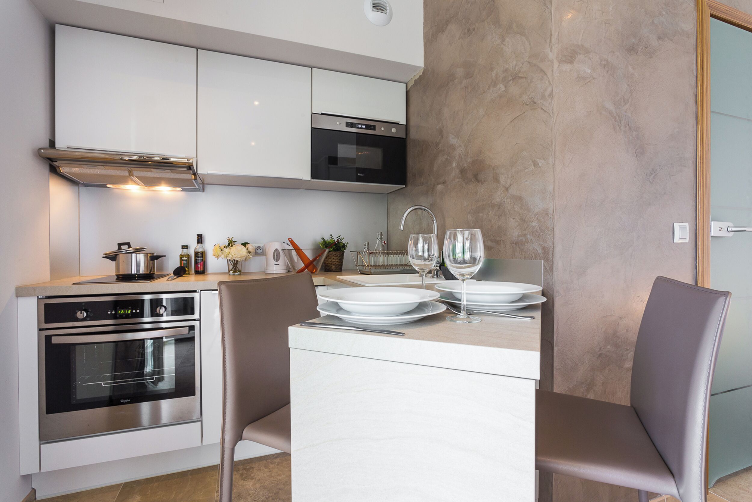 Una cocina moderna con electrodomésticos integrados, un comedor con una mesa dispuesta para dos personas y un amplio ventanal que proporciona luz natural.