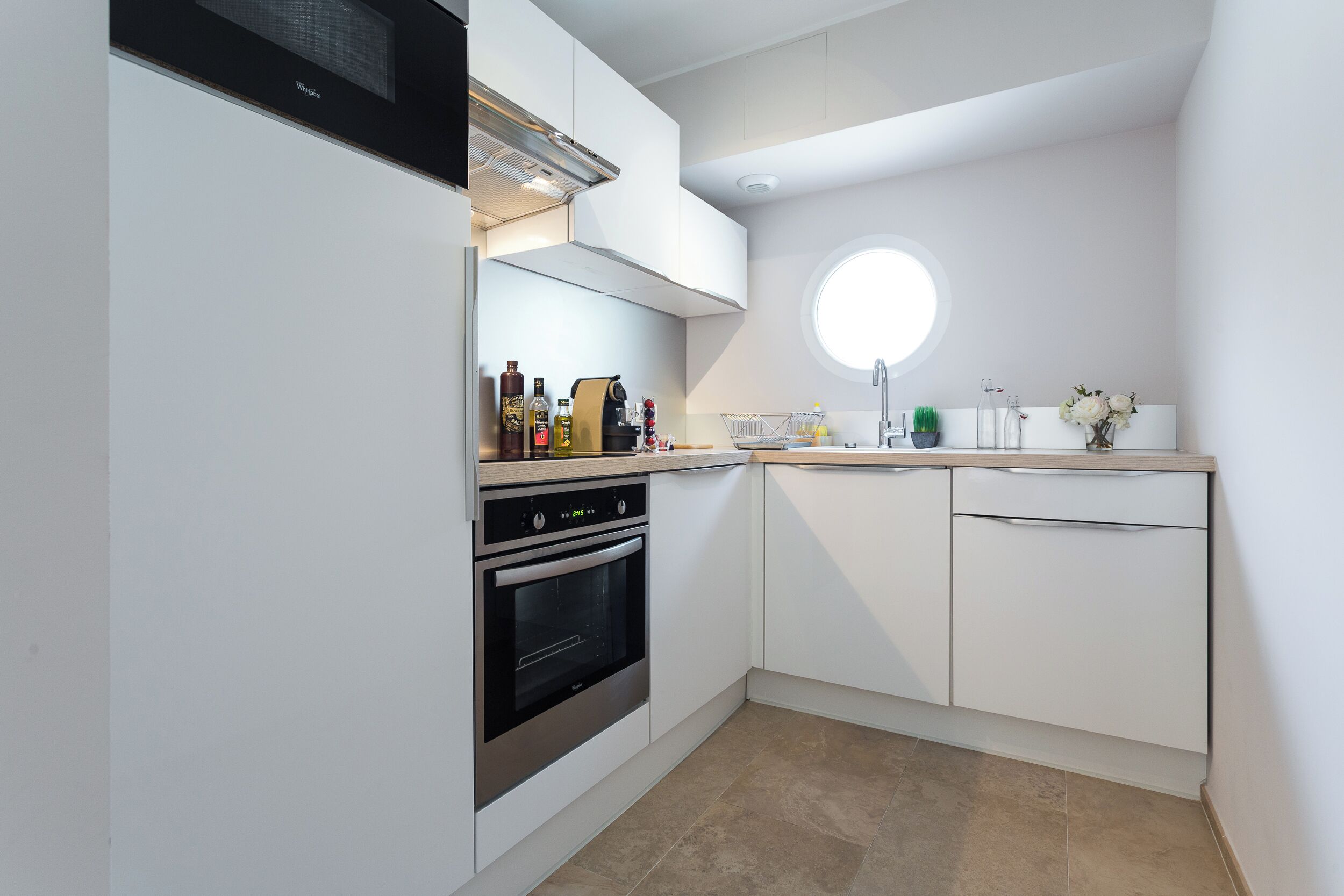 A modern kitchen with white cabinetry, a built-in oven, and a round window above the sink.