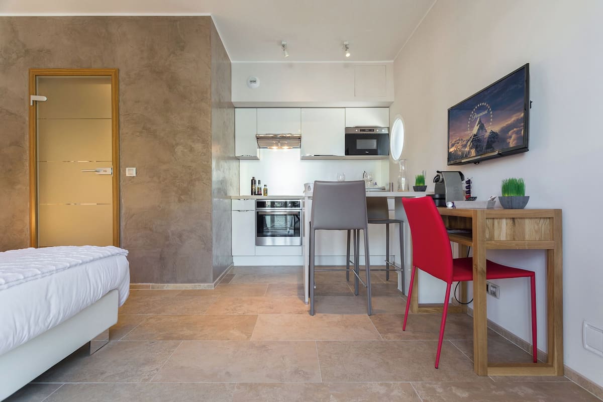 Une chambre d’hôtel compacte comprenant un lit, une kitchenette, un coin repas avec une table et des chaises, et un téléviseur fixé au mur.