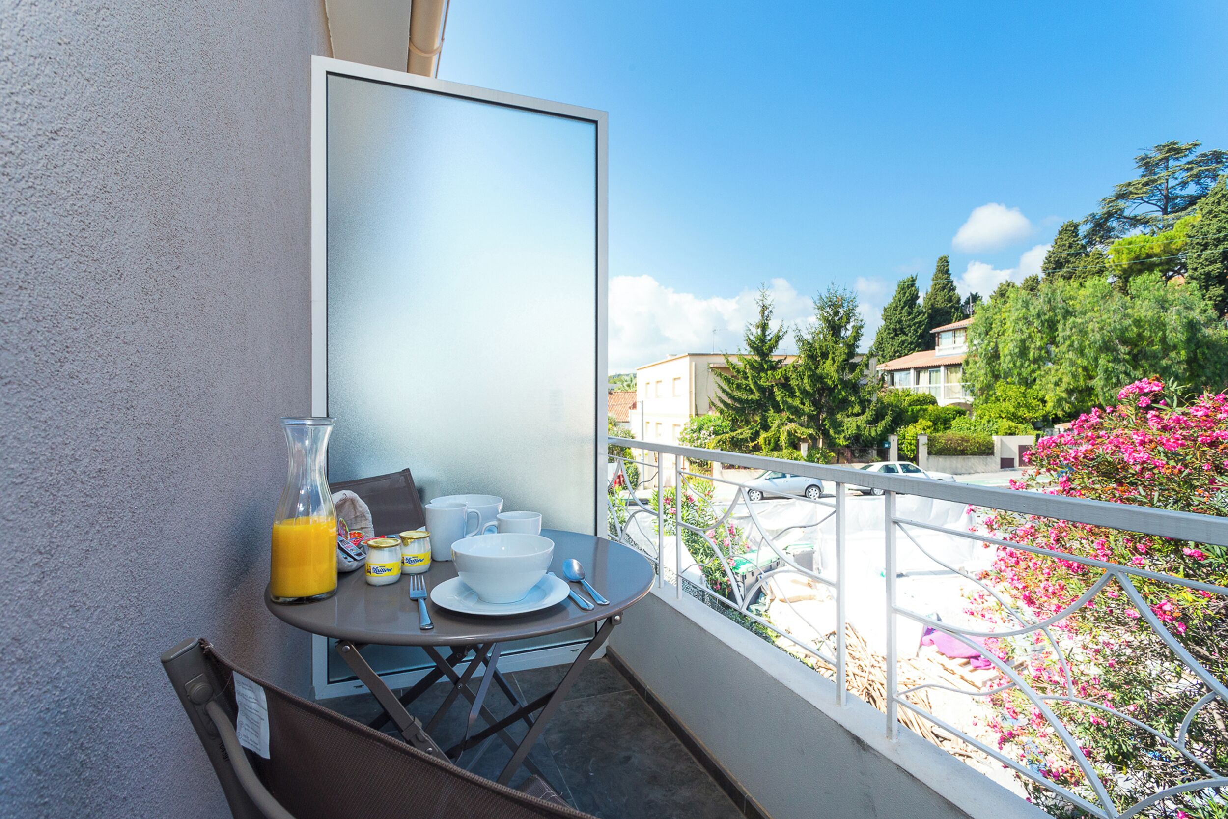 A balcony with a table set for breakfast, including a glass of orange juice, bowls, and utensils.