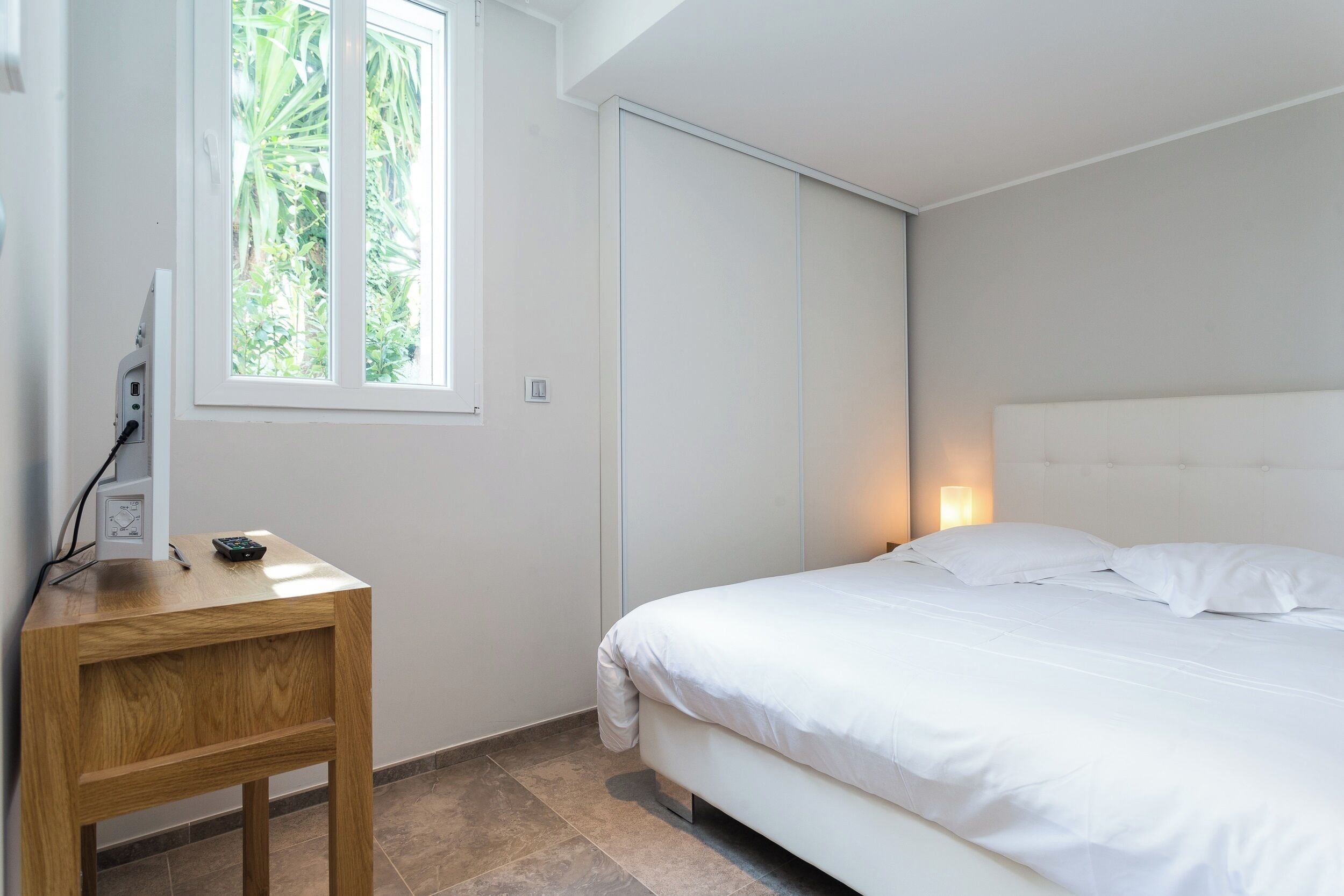 Una camera da letto con un letto, un comodino, una finestra e una lampada fissata al muro.