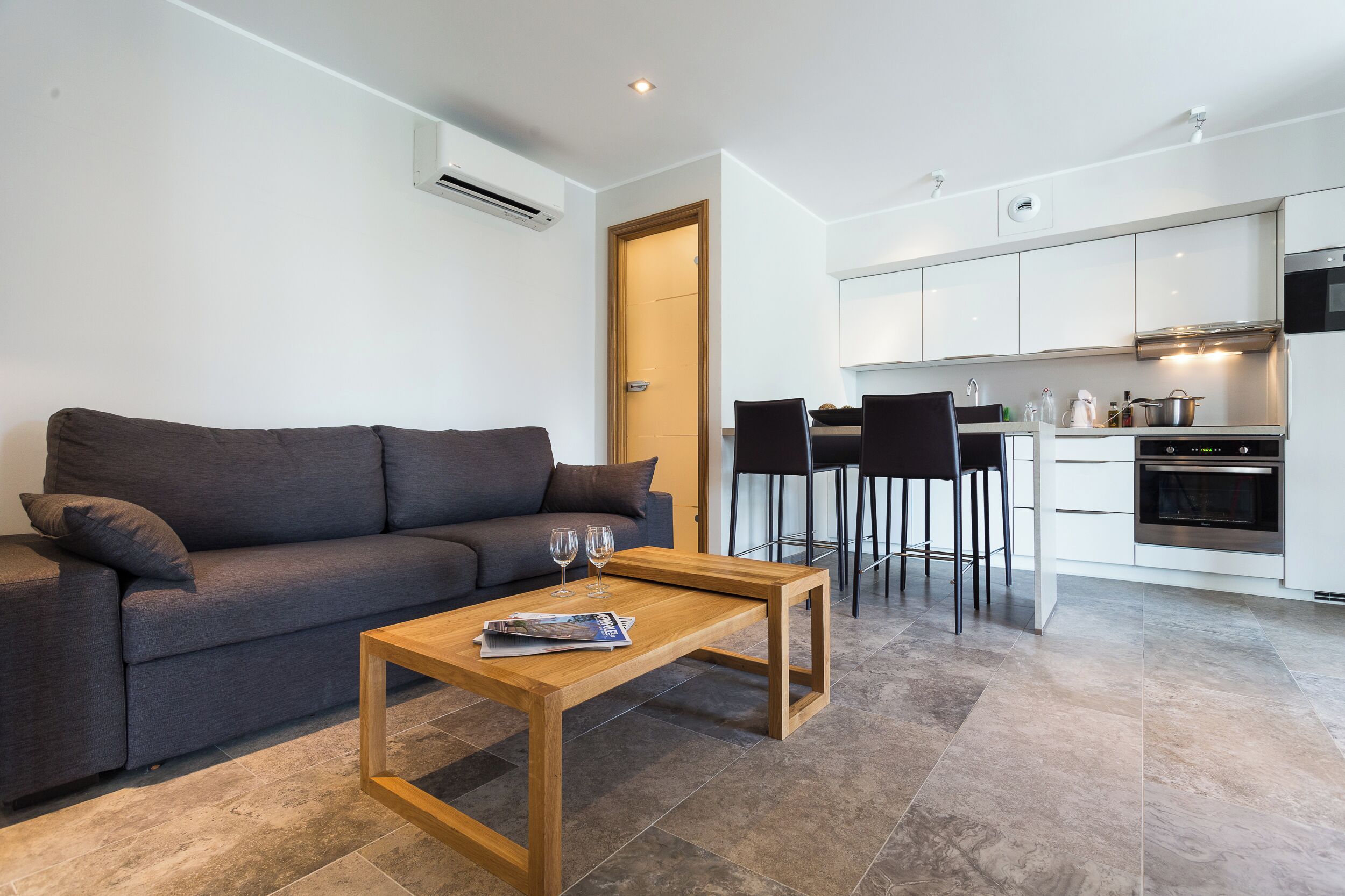 A modern living room with a sofa, coffee table, and kitchen area with white cabinets and a stove.