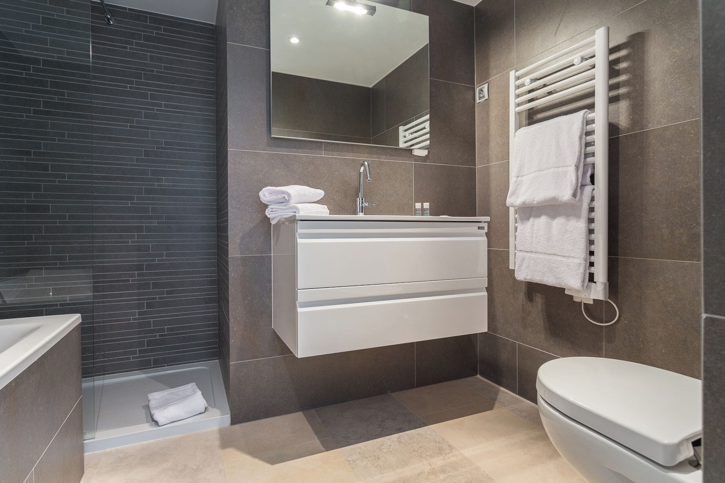 A modern bathroom with a bathtub, a sink with a mirror, and a toilet.