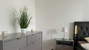 A modern bedroom with a grey wardrobe, a bedside table with a lamp, a black headboard, and a potted plant. - 2 Bedroom Apartment in Magdeburg (Magdeburg)