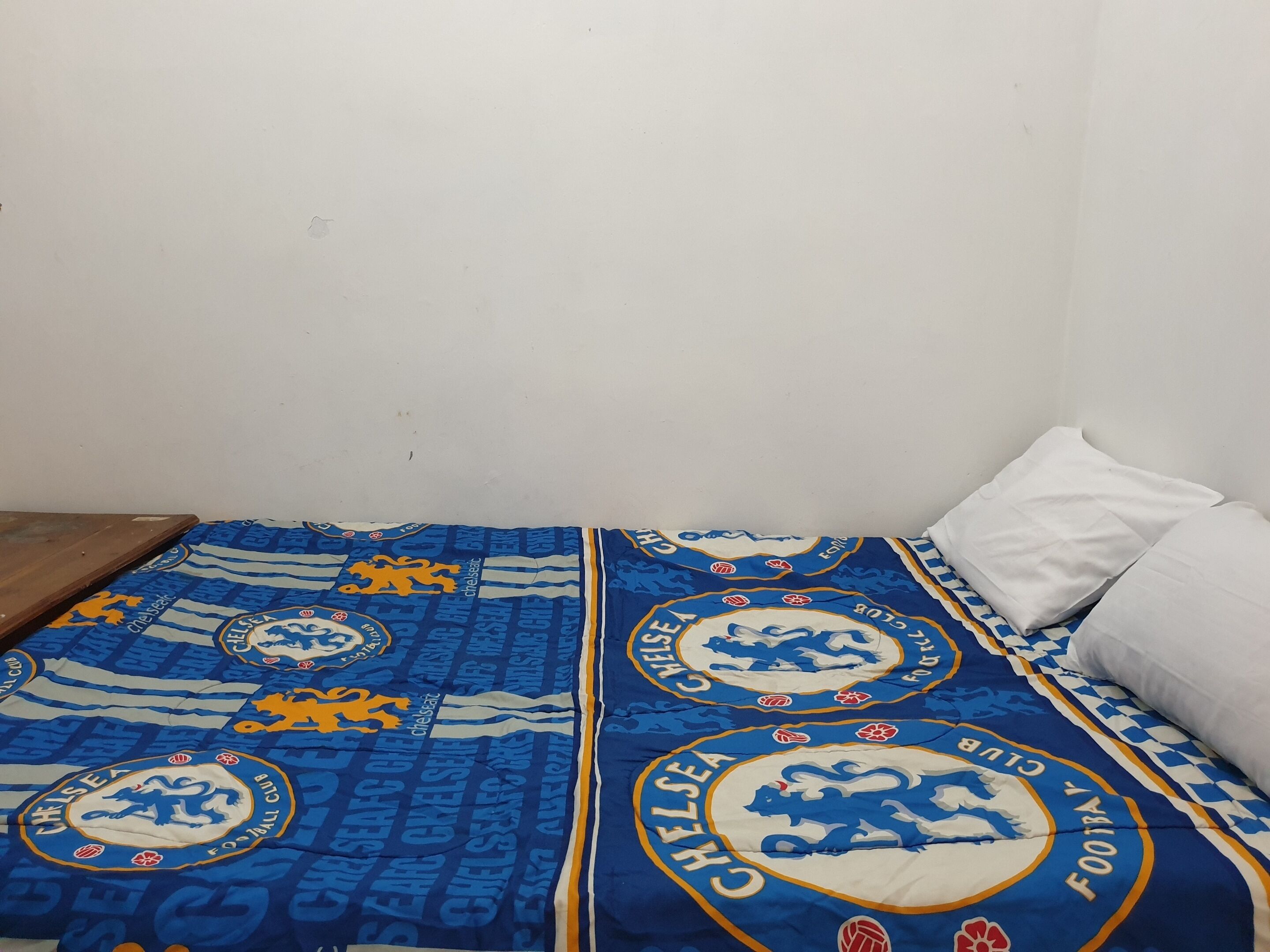 A bed with a blue Chelsea Football Club blanket and white pillows.