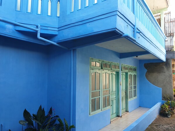 Un bâtiment bleu doté d’un balcon, d’une porte verte et d’un hall d’entrée carrelé.