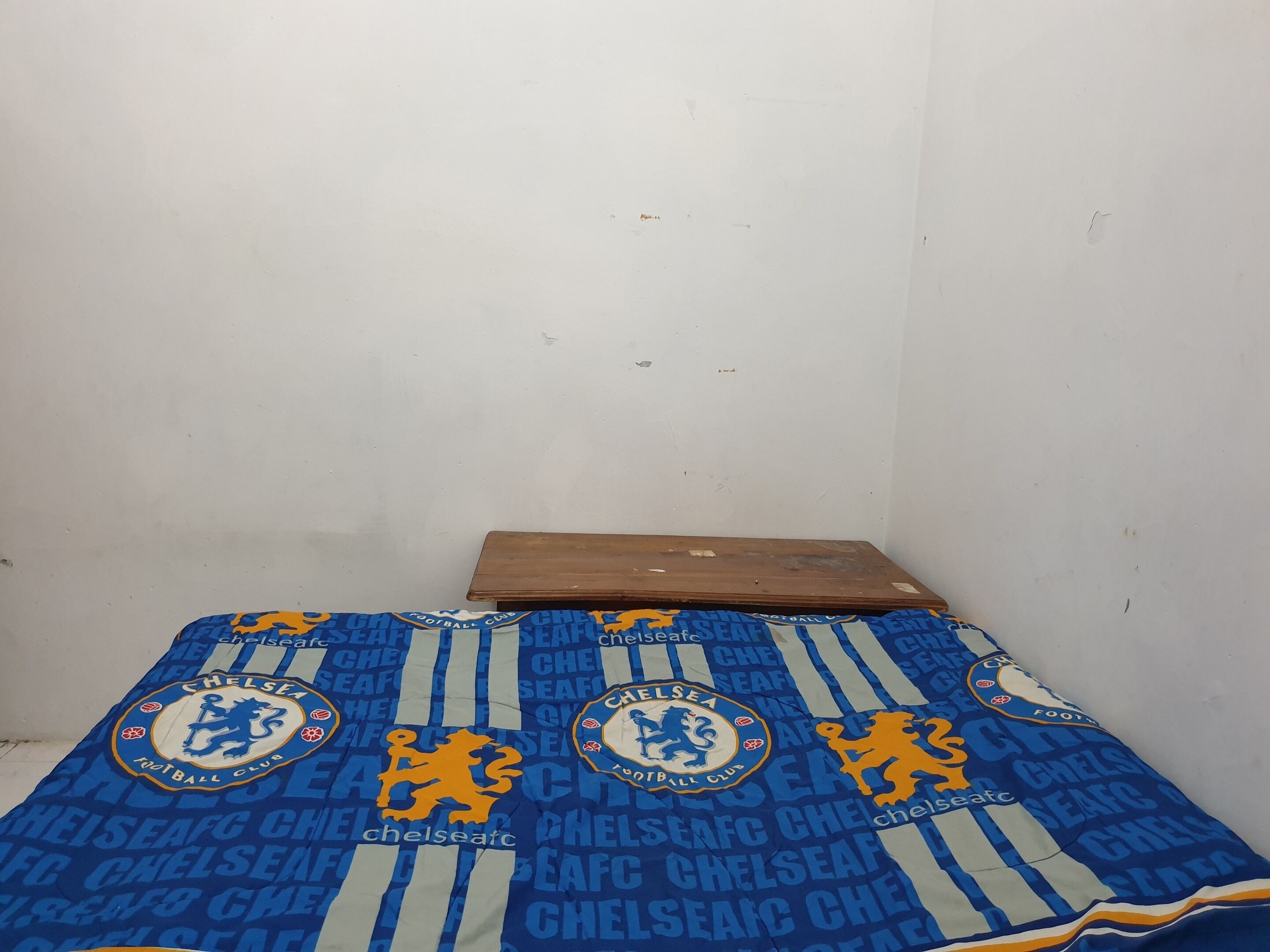 A small room with a bed covered in a Chelsea Football Club blanket.
