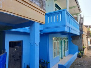 Un bâtiment bleu avec un balcon, une porte verte et une fenêtre avec des barreaux.
