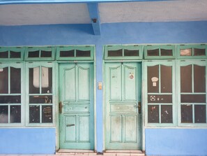 Fachada de edifício com duas portas verdes, numeradas 25 e 26, e várias janelas com sinais de desgaste.