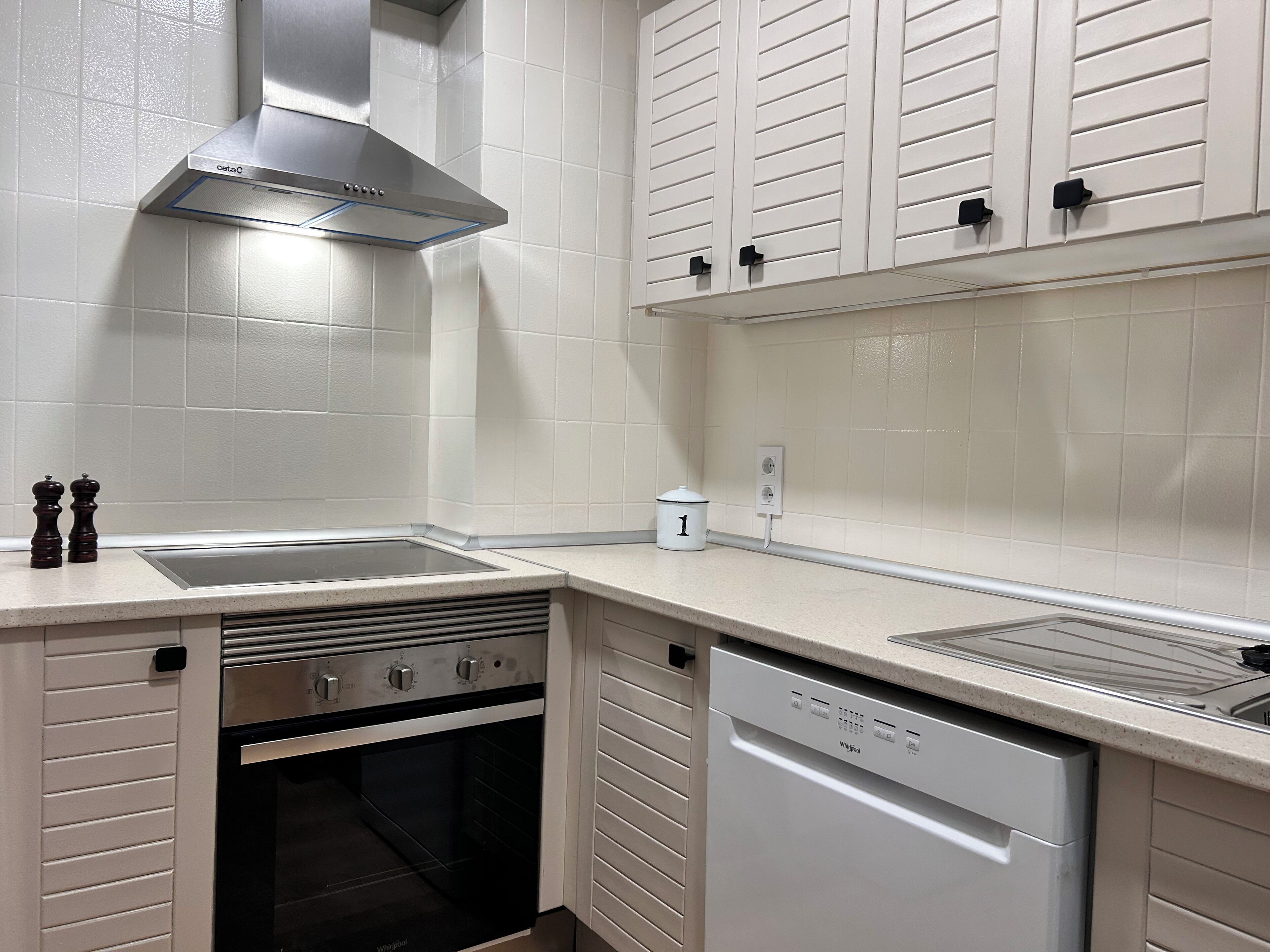 Una cocina moderna con armarios blancos, una campana extractora de acero inoxidable, horno empotrado y lavavajillas.