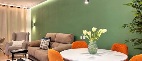 Un salon moderne avec un mur d’accent vert, une table ronde blanche, des chaises orange, un canapé marron et un tapis noir et blanc.