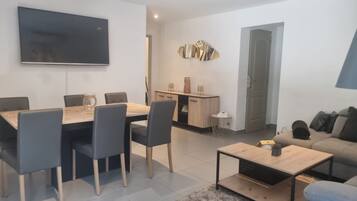 Una sala de estar moderna con comedor, cocina y televisor montado en la pared.