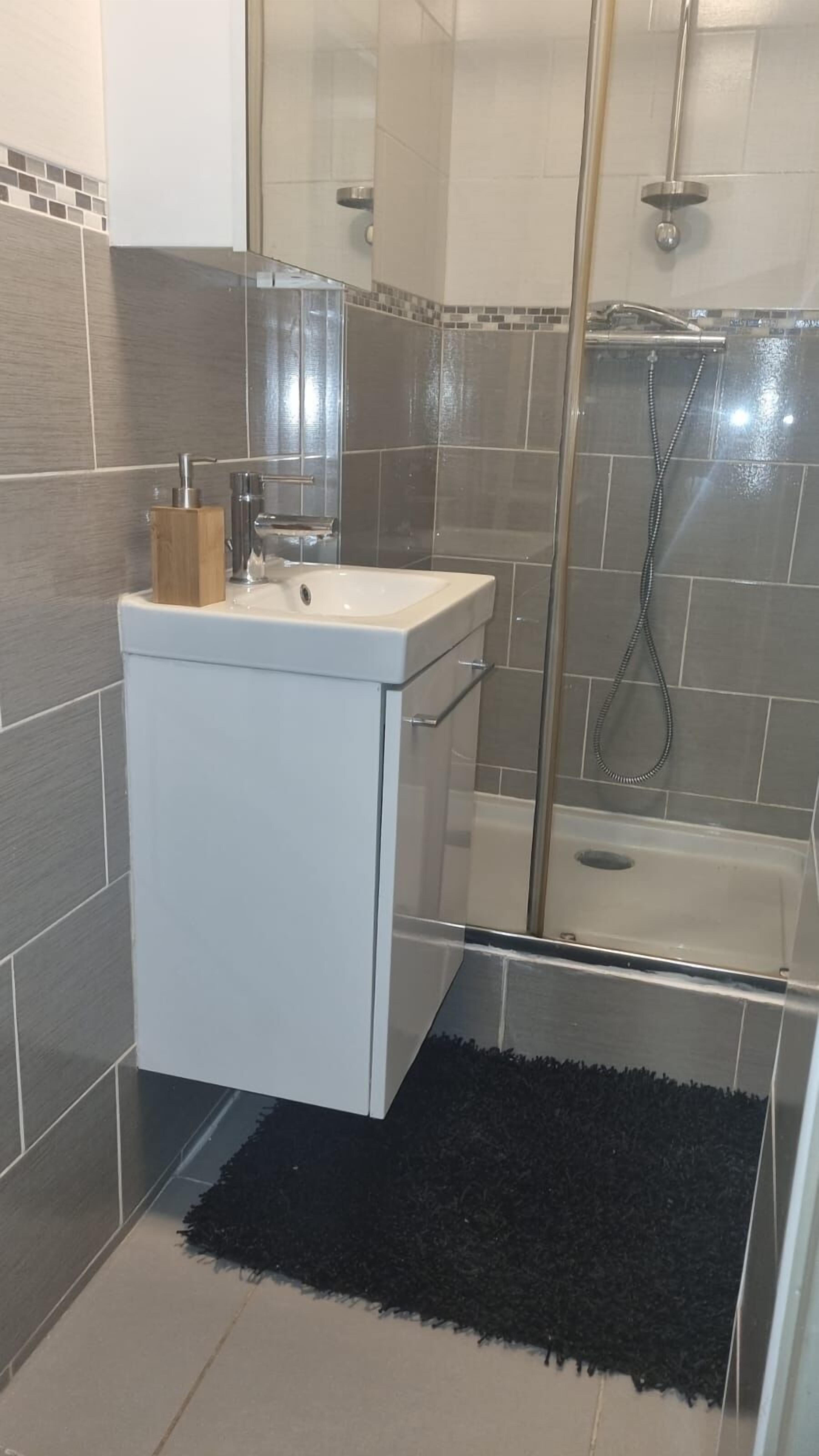 A modern bathroom with a white sink, a glass shower enclosure, and grey tiled walls.