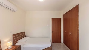 Un dormitorio con dos camas, una mesita de noche con lámpara, un armario de madera y un equipo de aire acondicionado.