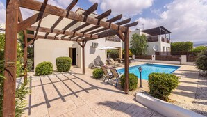 Zona junto a la piscina con pérgola, sillas de descanso y una pileta.
