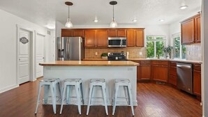 Cocina moderna con armarios de madera, electrodomésticos de acero inoxidable y una isla central con taburetes de bar.