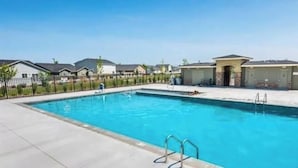 Una piscina con agua cristalina azul, rodeada por una valla y casas al fondo.