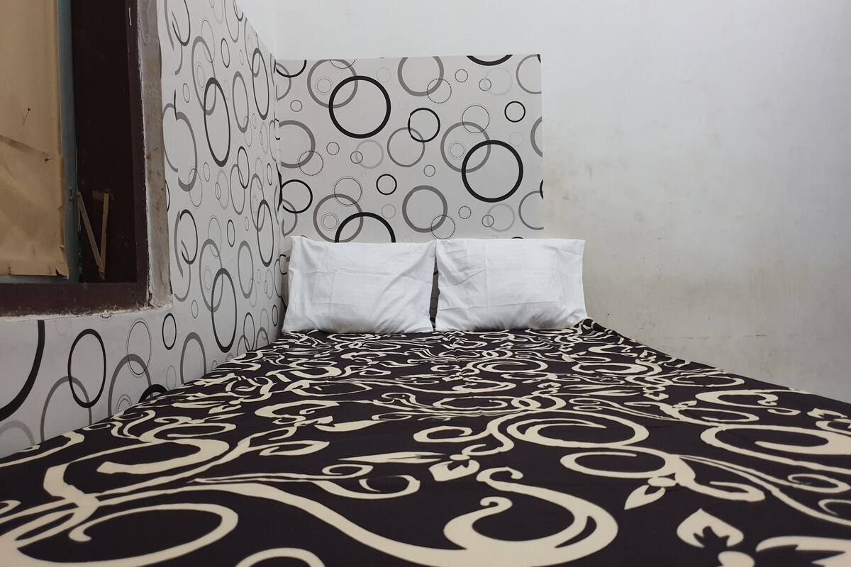 A bed with a black and white patterned bedspread, a white pillow, and a wall with a circular pattern.