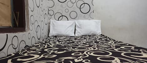 Una cama con una colcha de diseño blanco y negro, una almohada blanca y una pared con un motivo circular.